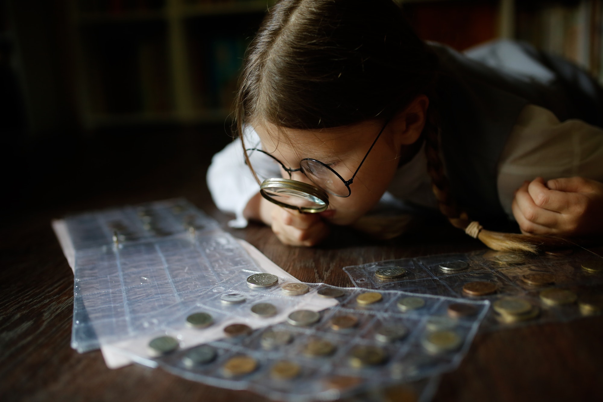 Kid in glasses with magnifying glass and collection of coins, numismatics, money